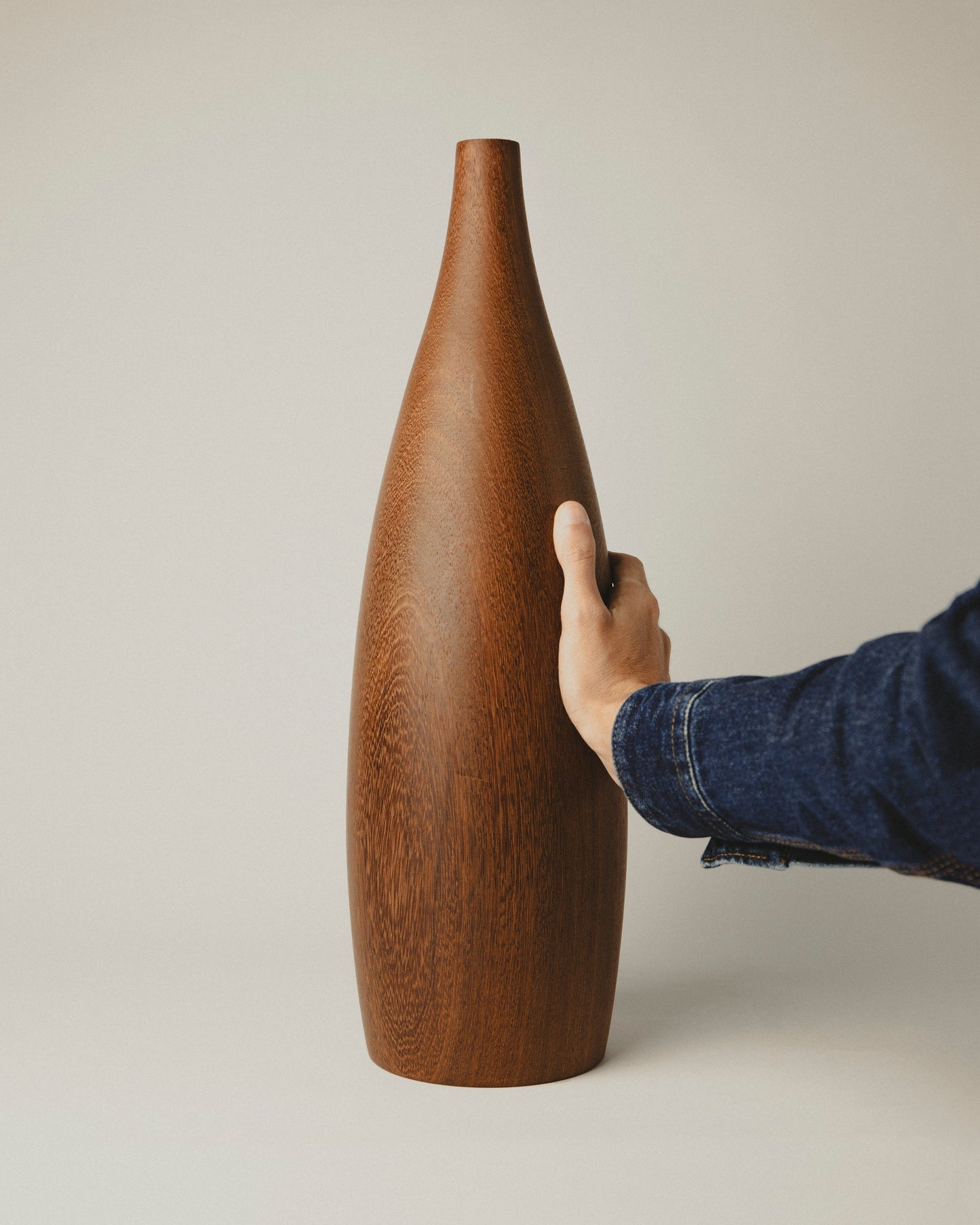 Jarrón decorativo de iroko hecho a mano. Modelo 05 con base sólida y cuerpo vertical. Foto con mano